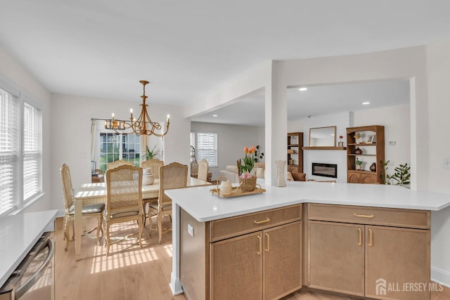 kitchen featuring a chandelier, light countertops, open floor plan, a glass covered fireplace, and light wood finished floors