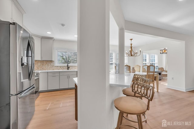 kitchen with decorative backsplash, light wood-style flooring, stainless steel appliances, light countertops, and a kitchen bar