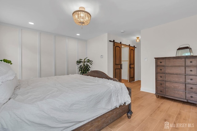 bedroom with light wood-style floors, recessed lighting, and a barn door