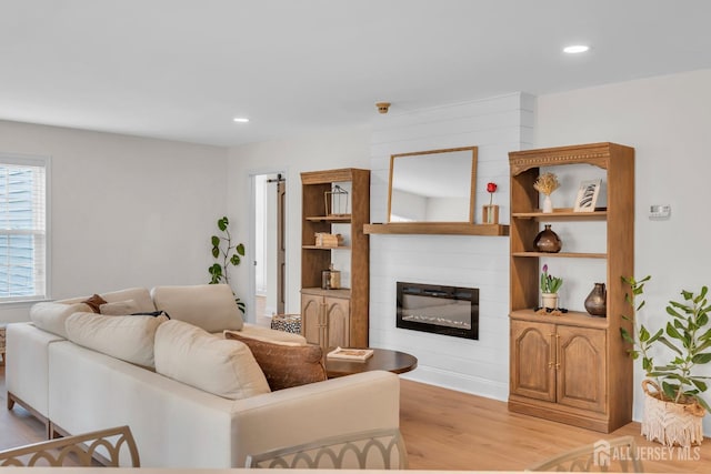 living room featuring recessed lighting, a large fireplace, and light wood-style flooring