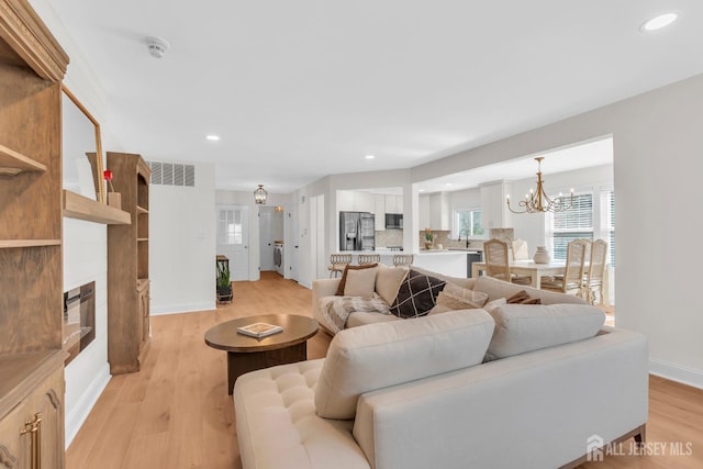 living room featuring light wood finished floors, recessed lighting, a chandelier, a fireplace, and baseboards