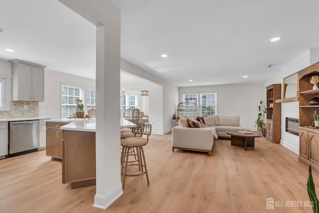 living room featuring recessed lighting, a glass covered fireplace, light wood-style flooring, and a healthy amount of sunlight