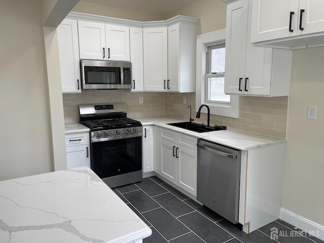 kitchen featuring dark tile patterned floors, a sink, white cabinetry, and appliances with stainless steel finishes