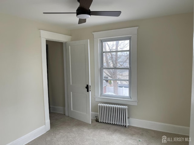 carpeted empty room featuring a ceiling fan, baseboards, and radiator