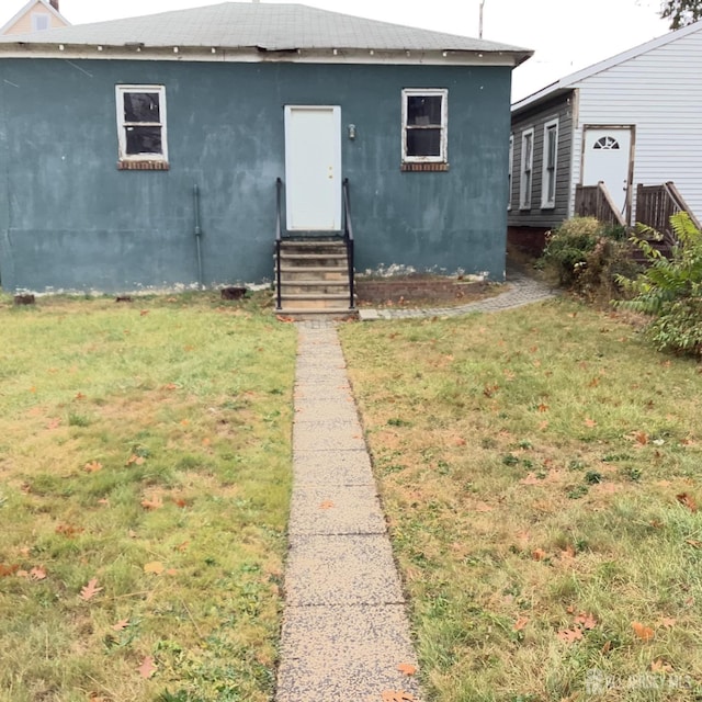 view of front of property with entry steps, a front lawn, and stucco siding