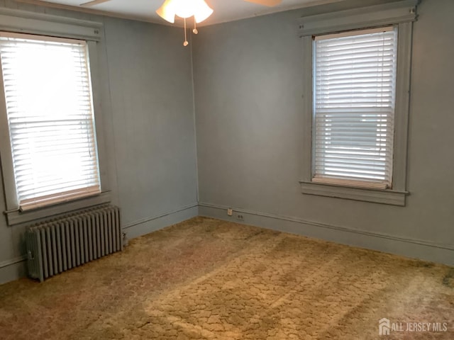 empty room featuring a ceiling fan, carpet floors, and radiator heating unit