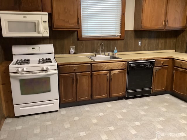 kitchen with white appliances, light countertops, a sink, and wood walls