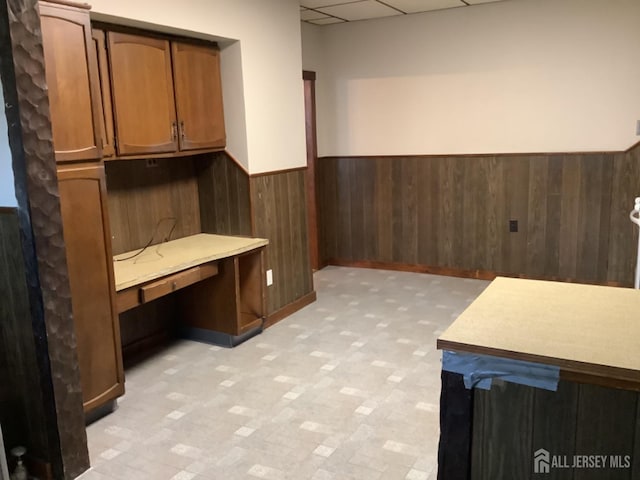 interior space with light floors, a wainscoted wall, wooden walls, and a drop ceiling