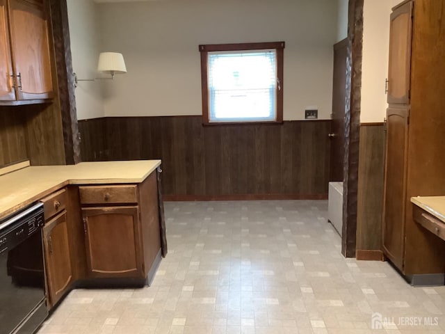 interior space featuring black dishwasher, wainscoting, a peninsula, light countertops, and wood walls