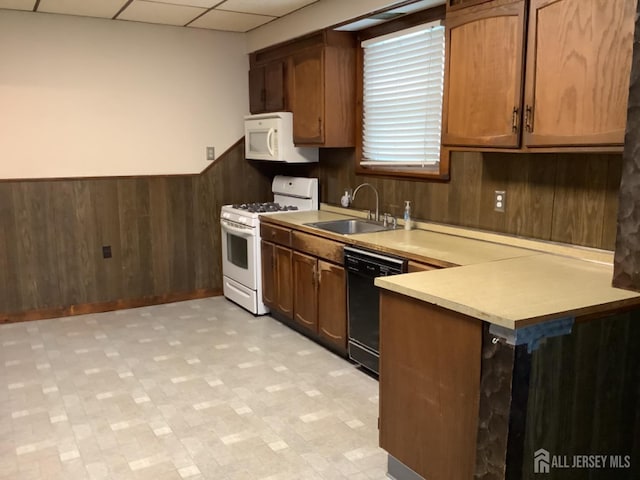 kitchen with white appliances, wainscoting, a paneled ceiling, wood walls, and a sink