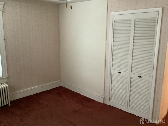 unfurnished bedroom with radiator, a closet, dark carpet, and wallpapered walls