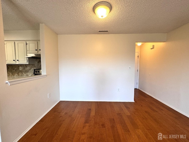 unfurnished room featuring a textured ceiling, dark wood-style flooring, baseboards, and visible vents