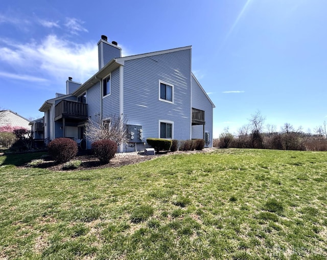 back of property featuring a balcony, a lawn, and a chimney