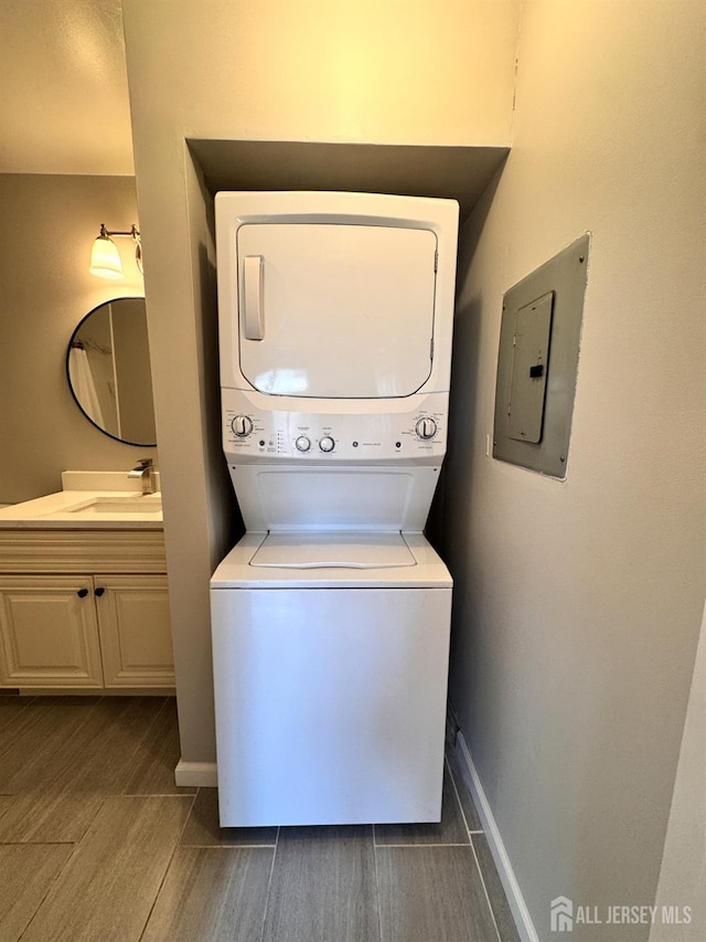 laundry area featuring electric panel, a sink, wood tiled floor, stacked washing maching and dryer, and baseboards