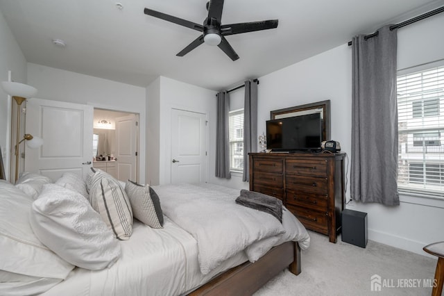 bedroom with a ceiling fan, light colored carpet, ensuite bath, and multiple windows