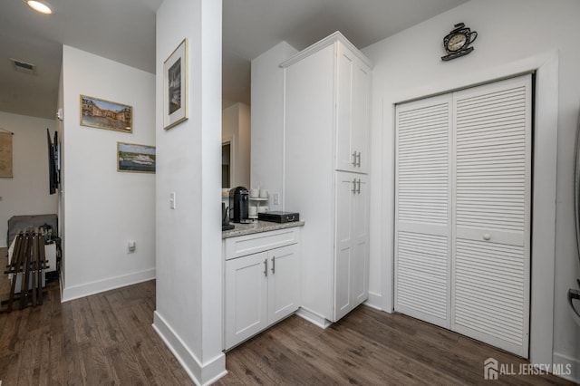 kitchen with baseboards, dark wood-style floors, white cabinetry, light stone countertops, and visible vents