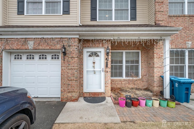 doorway to property with a garage and brick siding