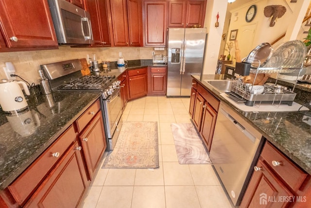 kitchen with stainless steel appliances, tasteful backsplash, dark stone countertops, and light tile patterned floors