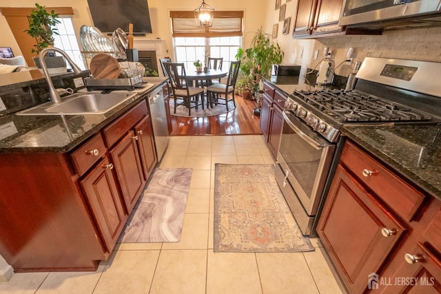 kitchen with light tile patterned flooring, a fireplace, a sink, appliances with stainless steel finishes, and decorative backsplash