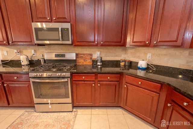 kitchen with light tile patterned floors, appliances with stainless steel finishes, dark stone counters, and tasteful backsplash