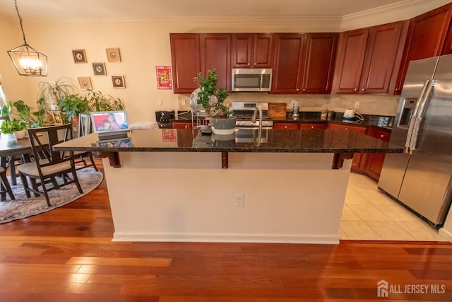 kitchen featuring a breakfast bar area, light wood-style flooring, ornamental molding, appliances with stainless steel finishes, and an island with sink