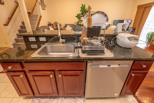 kitchen featuring a sink, dark stone countertops, stainless steel dishwasher, and light tile patterned flooring