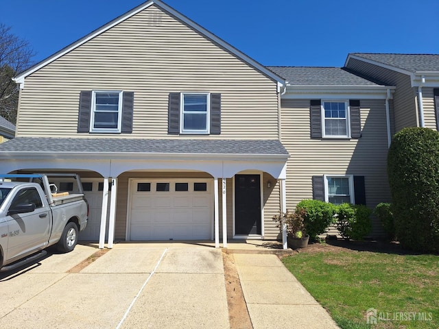 traditional home featuring an attached garage, concrete driveway, and roof with shingles