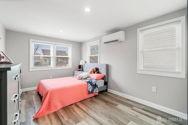 bedroom with multiple windows, an AC wall unit, baseboards, and wood finished floors