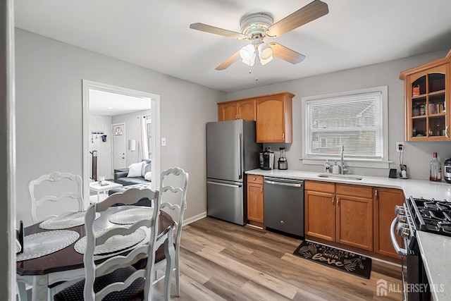 kitchen featuring light wood finished floors, glass insert cabinets, light countertops, appliances with stainless steel finishes, and a sink