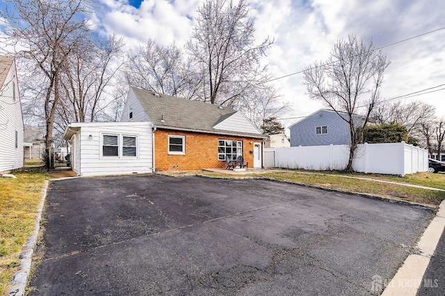 view of front of property featuring brick siding, aphalt driveway, and fence