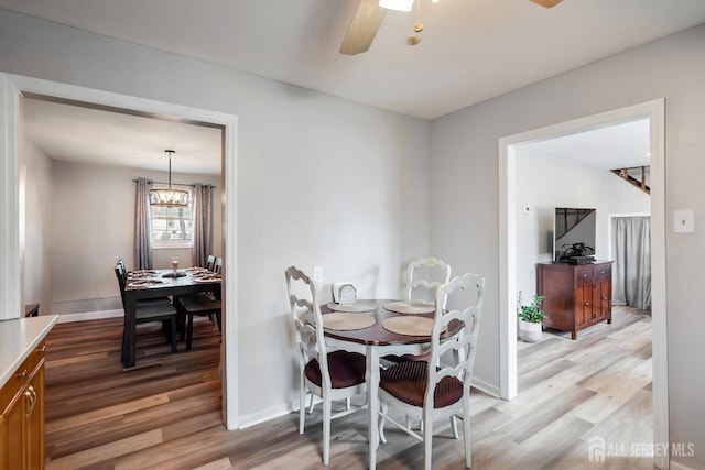 dining room featuring light wood-style flooring, ceiling fan with notable chandelier, and baseboards