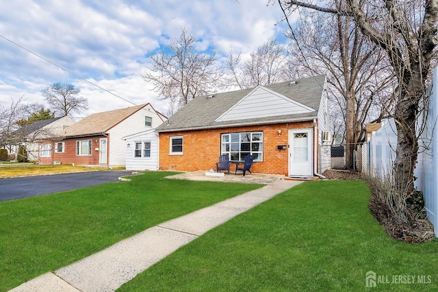 bungalow-style house featuring a front lawn, fence, brick siding, and roof with shingles