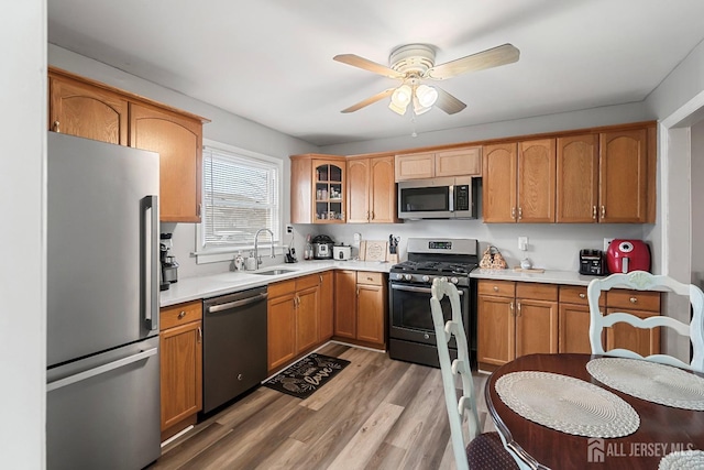 kitchen featuring a sink, stainless steel appliances, light wood-style floors, light countertops, and glass insert cabinets