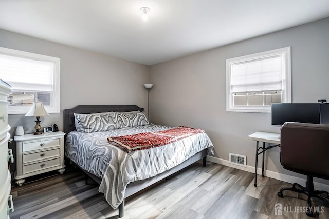 bedroom with multiple windows, wood finished floors, visible vents, and baseboards