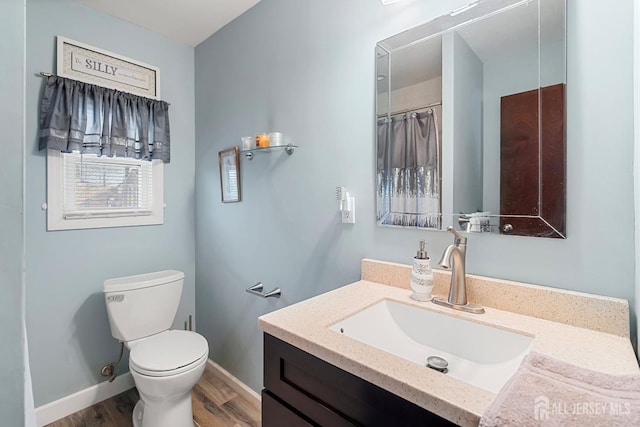 bathroom featuring baseboards, toilet, wood finished floors, and vanity