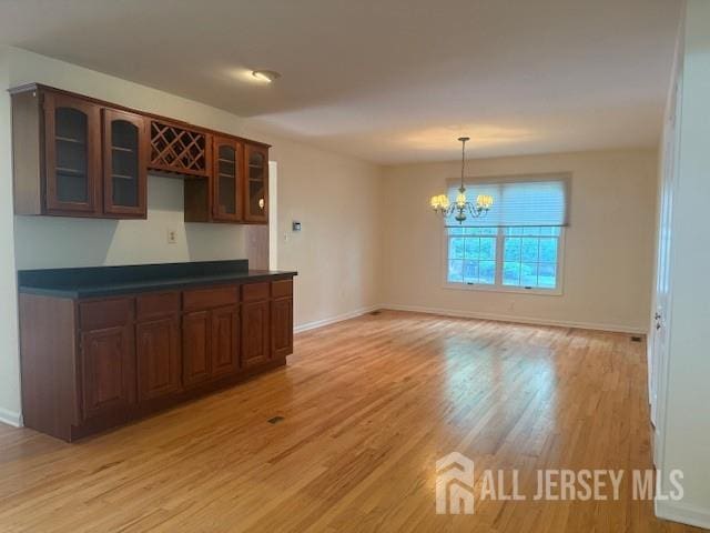 1 Cranberry Ct, South Brunswick, NJ 08540 - kitchen with a chandelier, glass insert cabinets, light wood-style floors, dark countertops, and pendant lighting