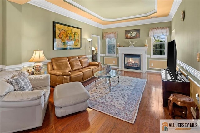 living room featuring a tray ceiling, a fireplace with flush hearth, hardwood / wood-style floors, and crown molding