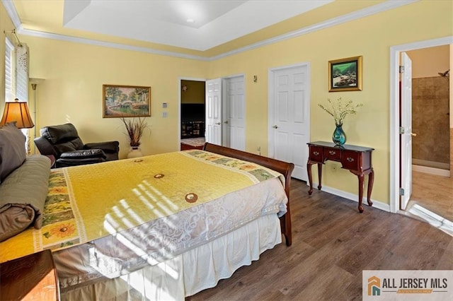 bedroom with baseboards, ornamental molding, a raised ceiling, and wood finished floors