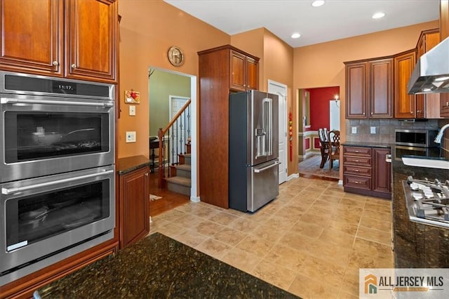 kitchen with stainless steel appliances, recessed lighting, decorative backsplash, dark stone counters, and wall chimney exhaust hood