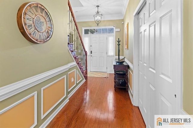 entryway featuring hardwood / wood-style flooring, a decorative wall, a wainscoted wall, a notable chandelier, and crown molding