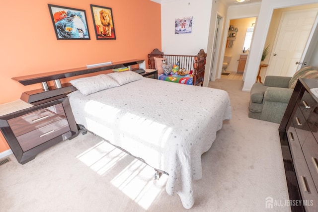 bedroom featuring light carpet, crown molding, and ensuite bathroom