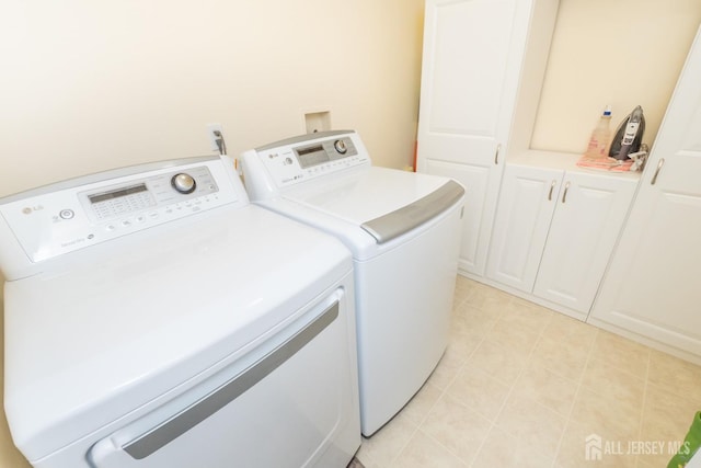 clothes washing area with cabinets, washer and dryer, and light tile patterned floors