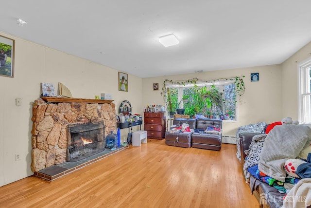 living room featuring hardwood / wood-style flooring, a baseboard heating unit, a stone fireplace, and a wealth of natural light