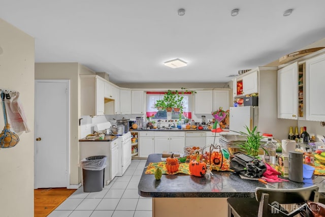 kitchen with light tile patterned flooring, sink, white cabinetry, kitchen peninsula, and white appliances