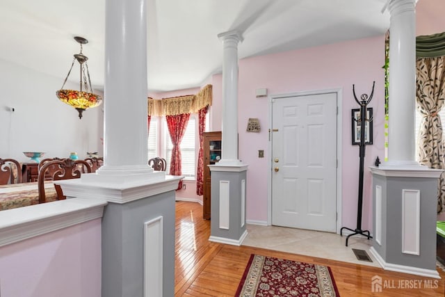 foyer entrance featuring light wood finished floors, visible vents, baseboards, and ornate columns