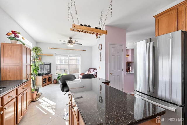 kitchen with dark stone countertops, open floor plan, a center island, freestanding refrigerator, and brown cabinetry