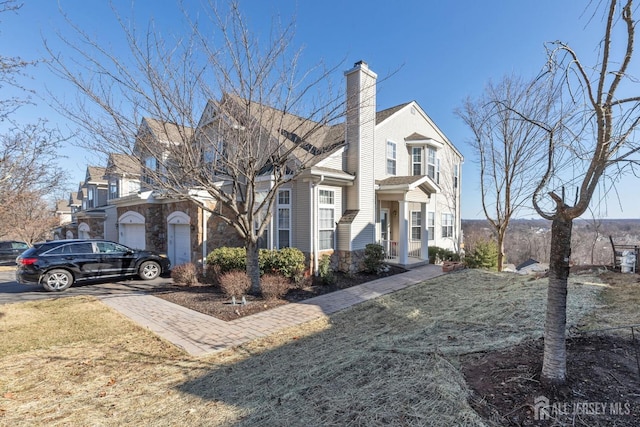 view of front of property featuring driveway, a front lawn, stone siding, a garage, and a chimney