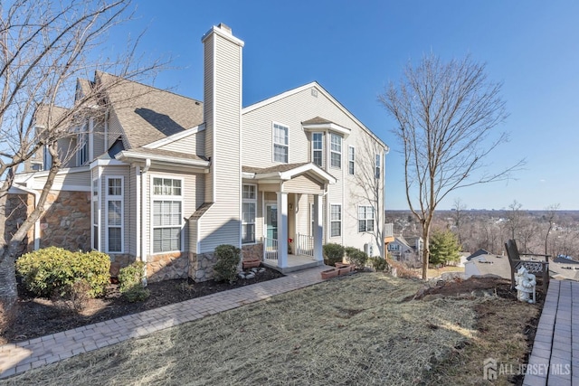 view of front of house with stone siding, a chimney, and a shingled roof