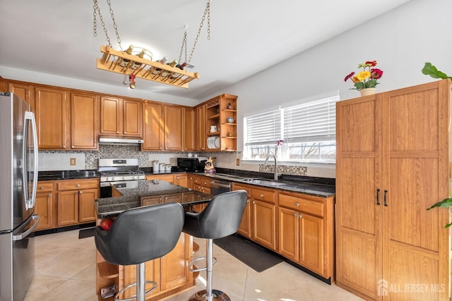 kitchen featuring under cabinet range hood, stainless steel appliances, brown cabinetry, and a sink