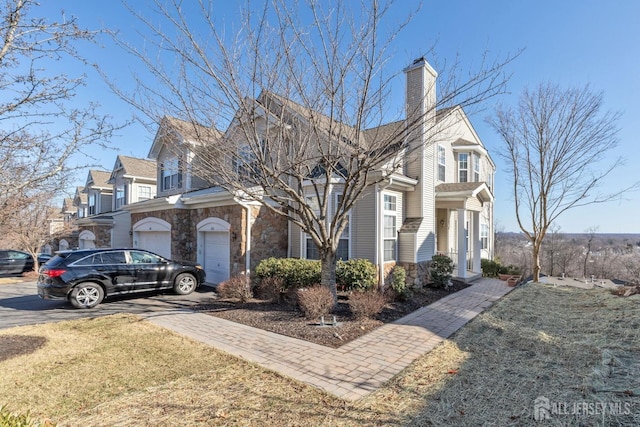 view of front of house with decorative driveway, stone siding, a residential view, a garage, and a chimney